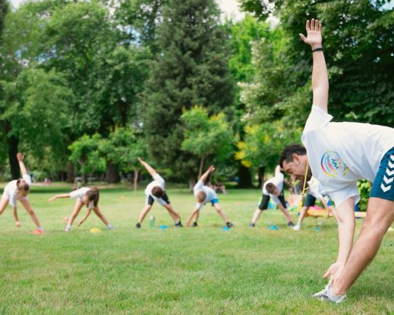 Kids stretching exercises in a park guided by a coach, promoting fitness and fun.